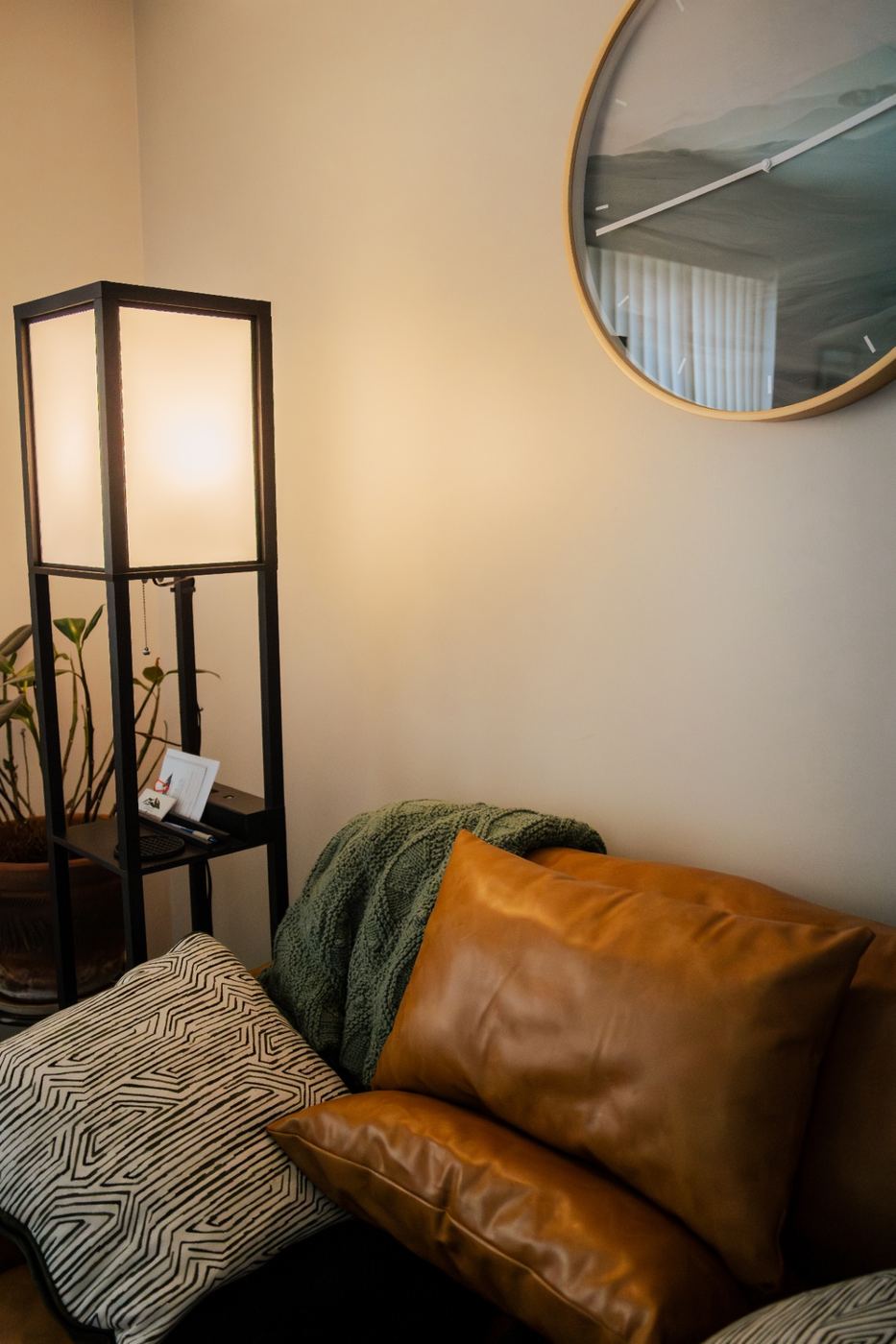 Cozy therapy nook with tan leather cushions, a warm floor lamp, and a framed landscape clock